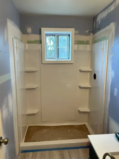 Bathroom mid-renovation showing a new shower surround with corner shelves and unfinished drywall walls.