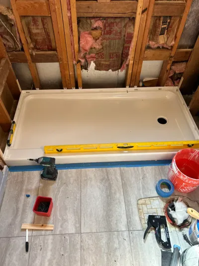 A shower pan being leveled and installed in a bathroom with exposed wall studs and insulation.