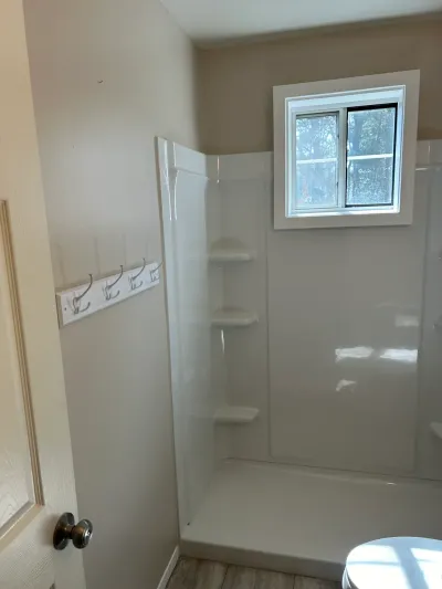 A finished bathroom shower stall with corner shelves and a window looking out to trees.
