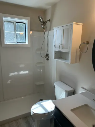 A finished bathroom with a corner shower, white wall cabinet, and navy blue vanity with white countertop.