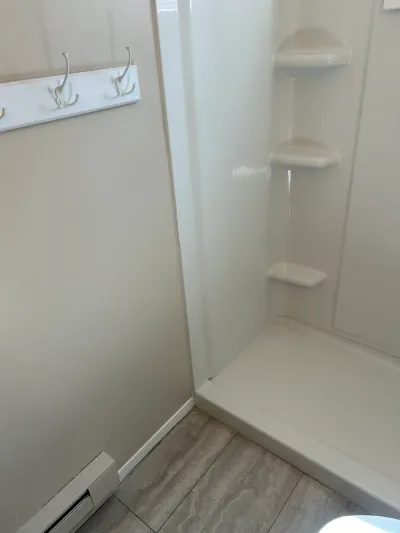 Corner of a bathroom with a built-in shower shelf unit, towel hooks on the wall, and tile flooring.