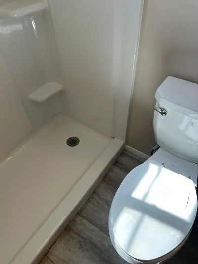 Finished bathroom with a white fiberglass shower stall, toilet, and wood-look vinyl plank flooring.