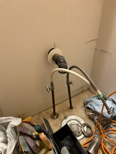 Exposed plumbing pipes and valves in a bathroom mid-renovation, surrounded by tools and debris.