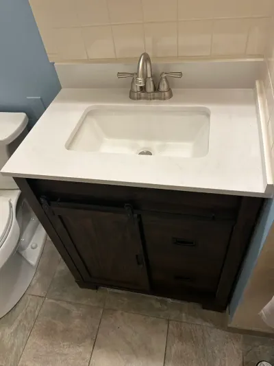 Finished bathroom vanity with white quartz counter, undermount sink, and dark wood barn-door style cabinet.