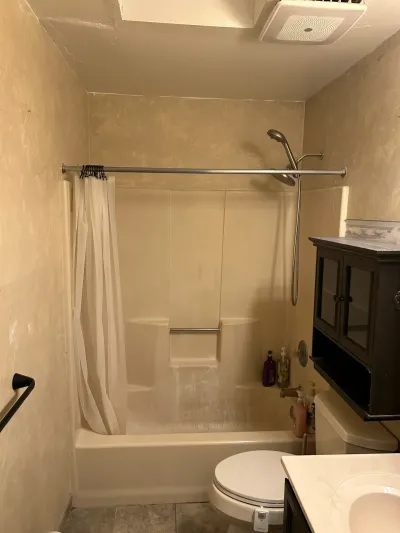 Dated bathroom with worn fiberglass tub-shower surround, toilet, and wall cabinet before renovation.