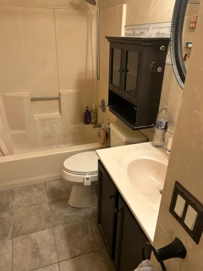 A cluttered, dated bathroom with a stained tub surround and dark vanity cabinets before renovation.