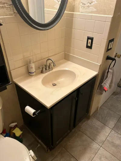 Dated bathroom vanity with cream tile, dark wood cabinet, and worn countertop before renovation.