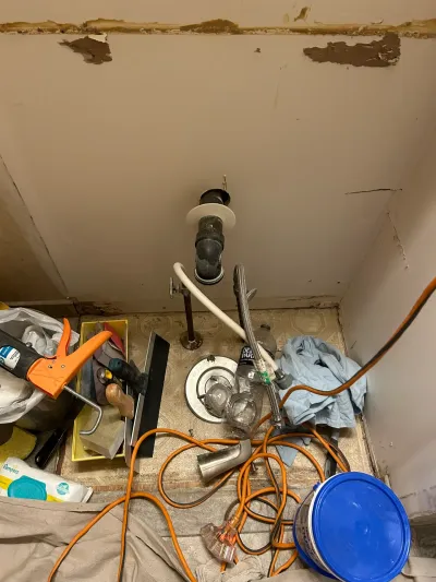 Close-up of exposed plumbing and water-damaged walls inside a bathroom sink cabinet during repair work.