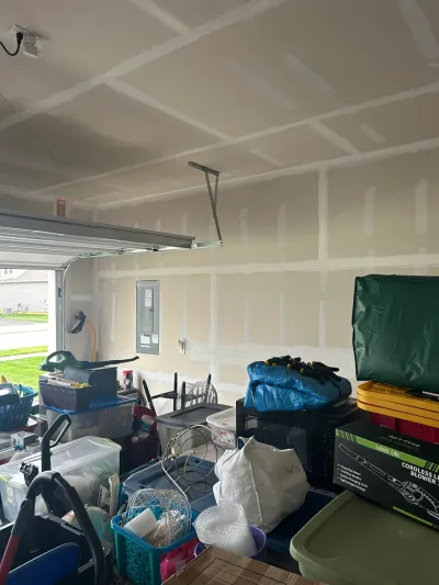 Garage interior with unfinished drywall seams on the ceiling and walls, cluttered with storage bins and tools.