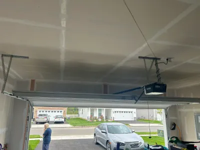Garage ceiling with fresh drywall taping and a newly installed garage door opener, viewed from inside with the door open.