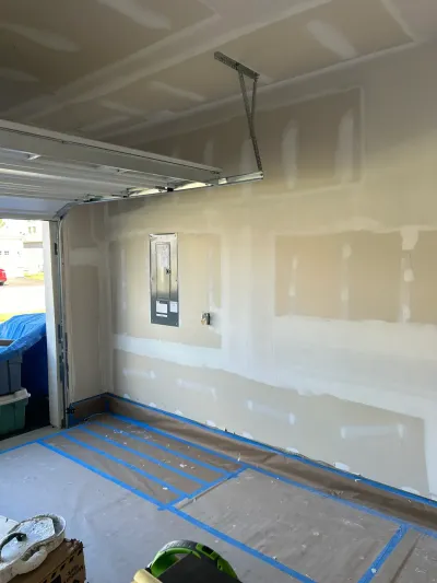 Garage under renovation with drywall seams being finished and floor protected by taped paper.