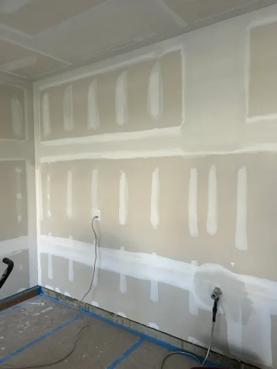 A room mid-renovation with drywall seams freshly mudded and an exposed electrical outlet on the wall.