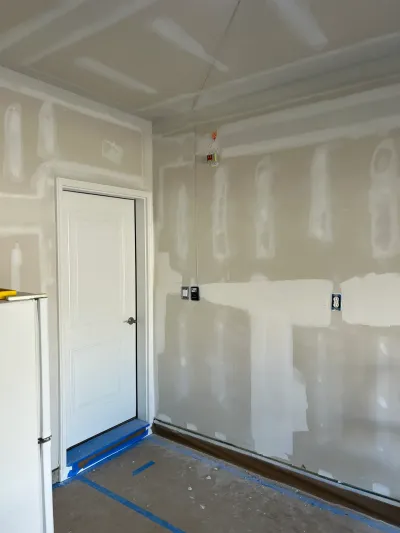 A room under construction with taped drywall seams, an installed white door, and exposed wiring awaiting fixtures.