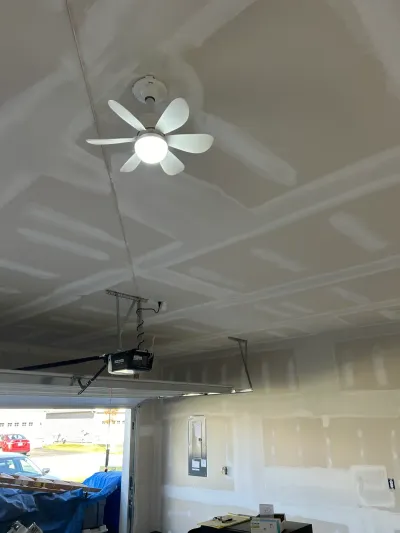 Garage ceiling with taped but unfinished drywall, a lit ceiling fan, and garage door opener visible.