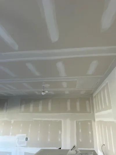 Ceiling and walls mid-drywall finishing with taped seams and a mounted ceiling fan, work still in progress.