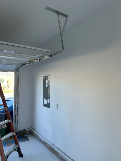 Garage under renovation with freshly painted walls, an electrical panel, and a ladder near the open door.