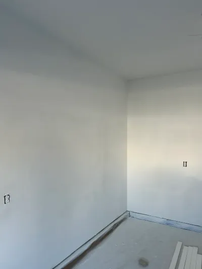 Unfinished room corner with primed drywall walls and bare concrete subfloor during renovation.