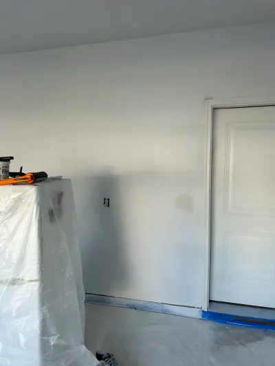 A room mid-renovation with a covered fixture, painter's tape, and a bare concrete floor.