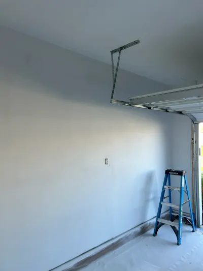 A garage under renovation with freshly painted walls, a step ladder, and the garage door track visible overhead.