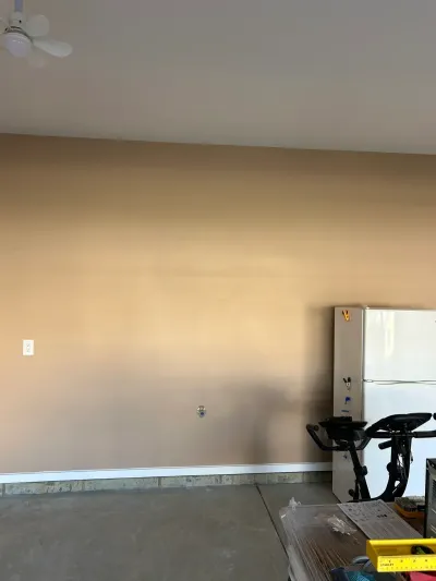 Empty basement room with tan walls, concrete floor, a refrigerator, and an exercise bike before renovation.