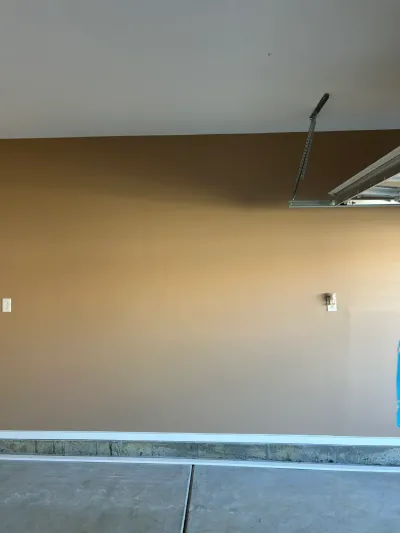 A tan garage wall with white trim, concrete floor, and part of the garage door track visible near the ceiling.