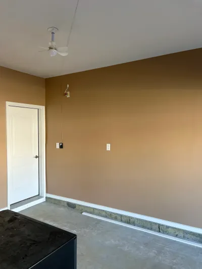 An unfinished basement room with tan painted walls, a concrete floor, and a ceiling fan installed.