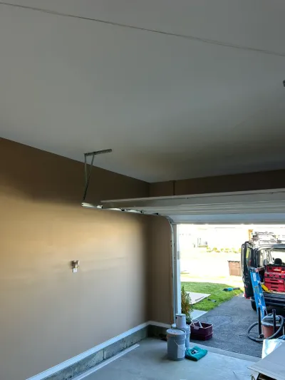 Garage with a newly painted tan wall and white ceiling, door open to a driveway with a work van outside.