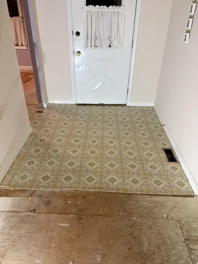 Entryway floor mid-demolition showing old patterned vinyl partially removed to expose the plywood subfloor.