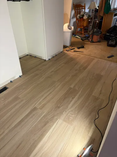 New wood-look vinyl plank flooring being installed in a basement, transitioning into old carpet with tools scattered nearby.