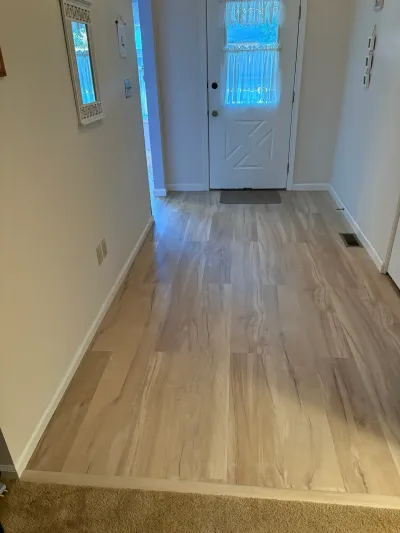 Hallway with new wood-look vinyl plank flooring leading to a white front door with a decorative window.