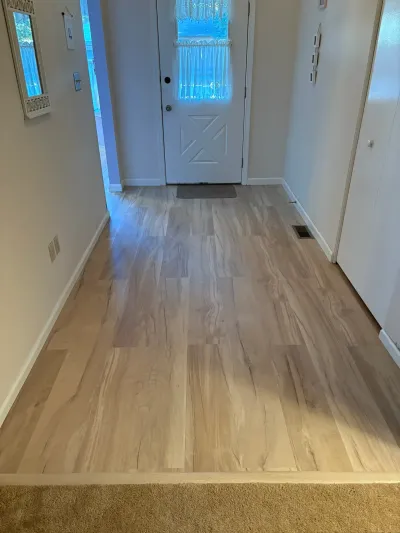 Hallway with new light wood-look vinyl plank flooring leading to a white front door.