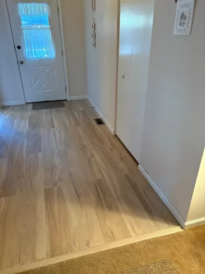 Hallway entryway with new light wood-look vinyl plank flooring leading to a white front door.