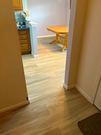 Hallway view into a kitchen and dining area with new wood-look flooring and oak cabinetry.