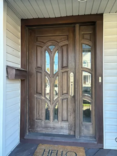 A stained wood front door with arched glass panels and a matching sidelight, set on a covered porch.