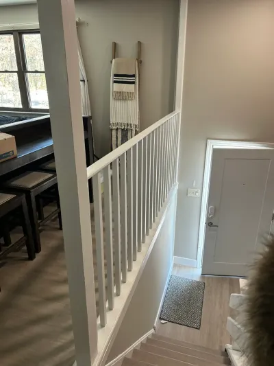 A white-railed staircase overlooks a dining nook and entryway with light wood flooring.
