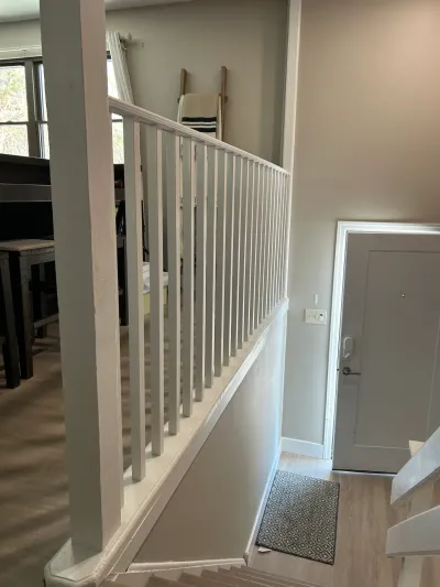 Staircase with white painted railing overlooking an open living area, next to a gray entry door.