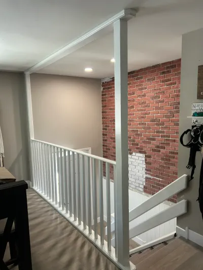 Landing with white railings overlooks a staircase beside a partially finished exposed brick accent wall.