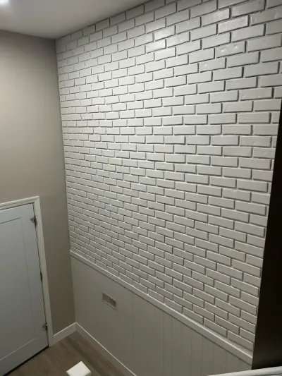 Basement corner with a painted white brick accent wall above beadboard wainscoting and a paneled door.
