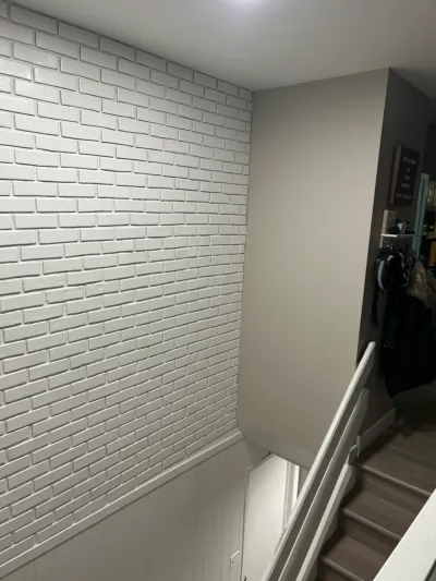 A stairwell with a white-painted brick accent wall descending to a lower level with coat hooks and jackets.