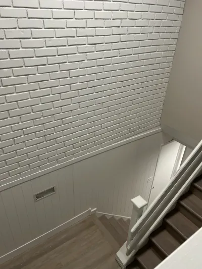 Stairwell with a white painted brick accent wall, beadboard wainscoting, and dark wood stair treads.