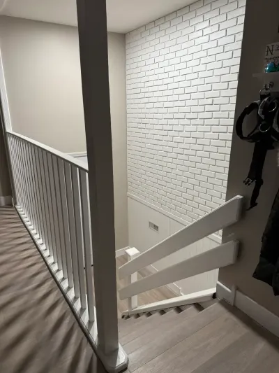 An upper hallway landing overlooks a staircase with white railings and a painted white brick accent wall.