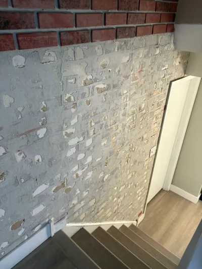 A brick basement stairwell wall midway through patching and skim-coat repair above finished stairs.