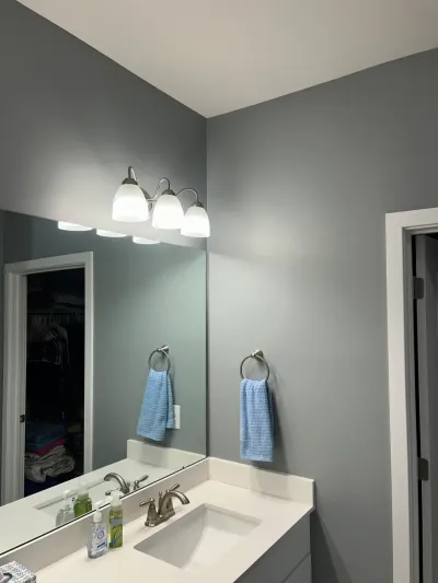A gray bathroom vanity with a large mirror, brushed nickel fixtures, and a blue hand towel.