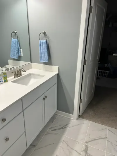 White vanity with quartz counter, brushed nickel fixtures, and marble-look tile floor in a finished bathroom.