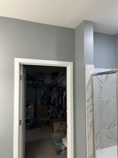 Gray bathroom corner with a marble-tile walk-in shower next to an open walk-in closet doorway.