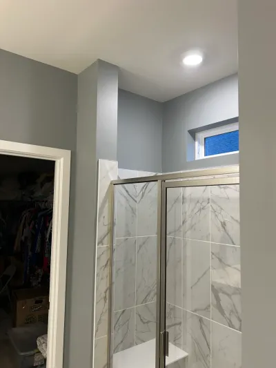Finished bathroom shower with marble-look tile and glass door, next to a walk-in closet.
