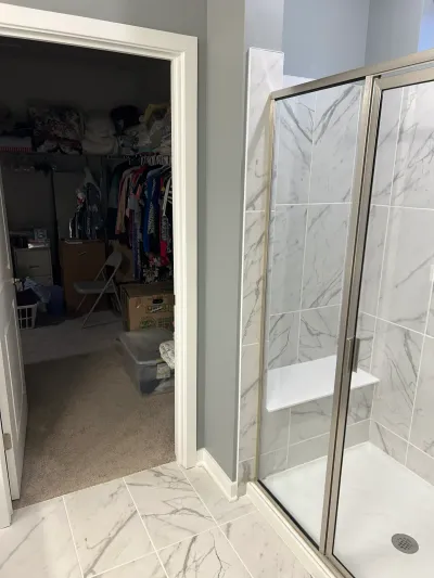 Finished bathroom with a marble-tile walk-in shower and glass door next to an open walk-in closet.