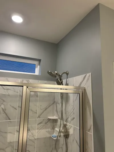 Close-up of a tiled shower with glass door, dual shower heads, and a window under a sloped ceiling.