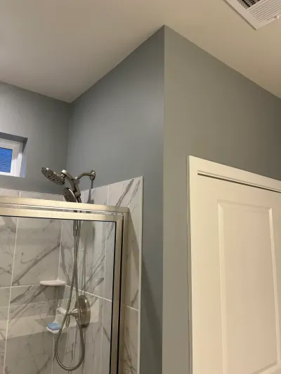 Corner shower with marble-look tile, glass door, and brushed nickel fixtures against a slate blue accent wall.
