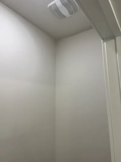 Close-up of a painted bathroom corner with a ceiling-mounted exhaust fan vent.